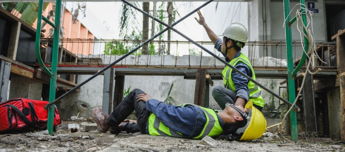 An injured construction worker lying on the ground next to scaffolding while a supervisor gestures for help at a building site.