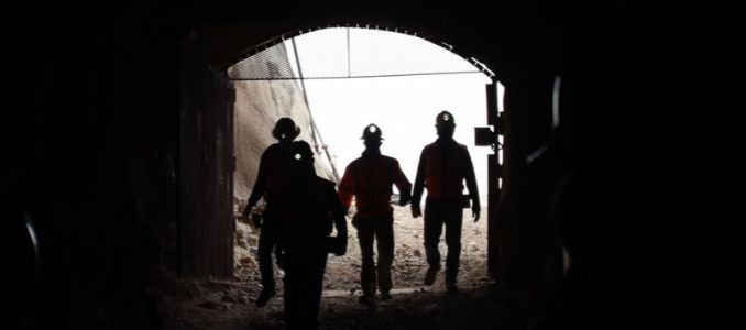 Three workers wearing headlamps enter a mine.