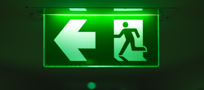 Illuminated green emergency exit sign with a left-pointing arrow and a running person symbol.