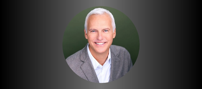 Headshot of Randy Fiser, incoming AIHA CEO, smiling in a gray blazer and white open-collar shirt against a dark green background. Photo: Jeff Kurysz.