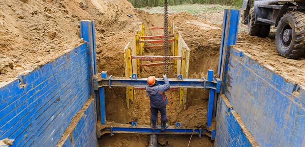 worker pulling on chain while standing in trench that has blue and yellow trench supports