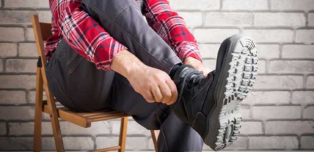 person sitting in red flannel shirt and grey jeans while putting on black boots