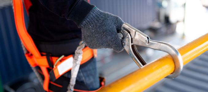 Worker attaches a safety harness lanyard to a metal railing for fall protection.