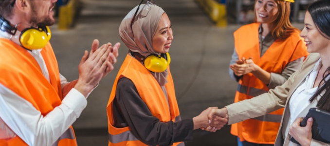 A worker shaking hands with an executive, as colleagues applaud.