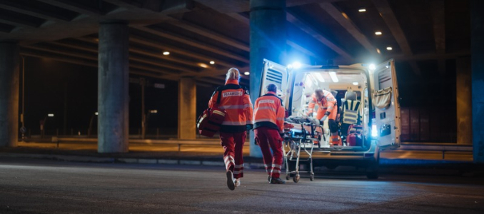 Paramedics in high-visibility uniforms rushing toward an open ambulance with a stretcher under an overpass at night.