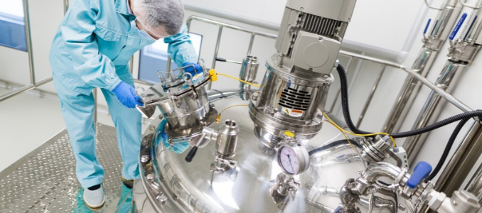 A worker wearing protective clothing, a hairnet and blue gloves operates stainless steel processing equipment in an industrial facility.